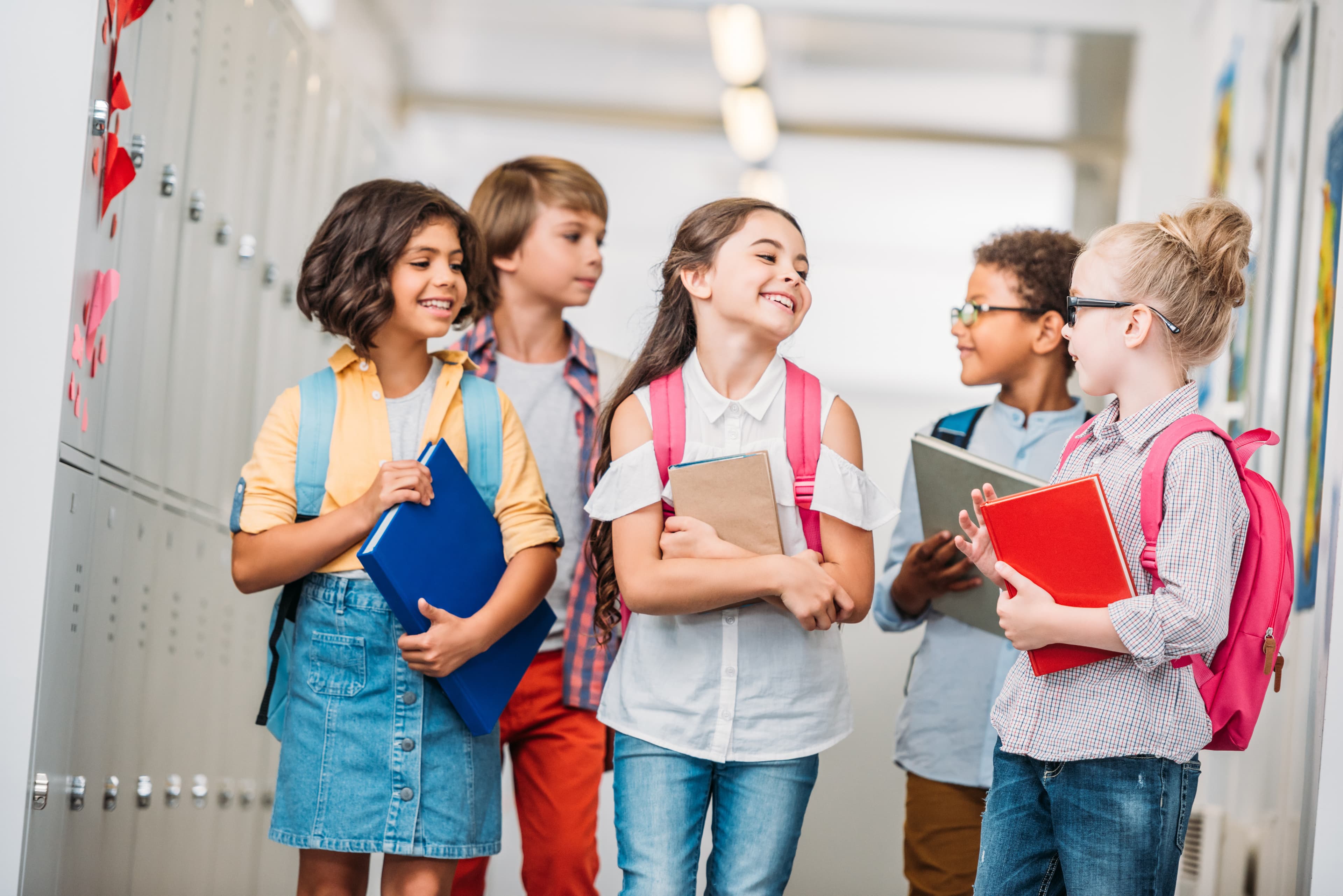 Group of kids walking together in the school hallway with backpacks and books.